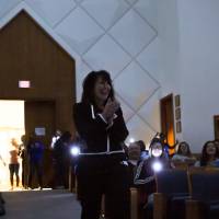 Image of President Mantella's entrance into program. Students use phone flashlights to light the aisle as she walks in to dark room